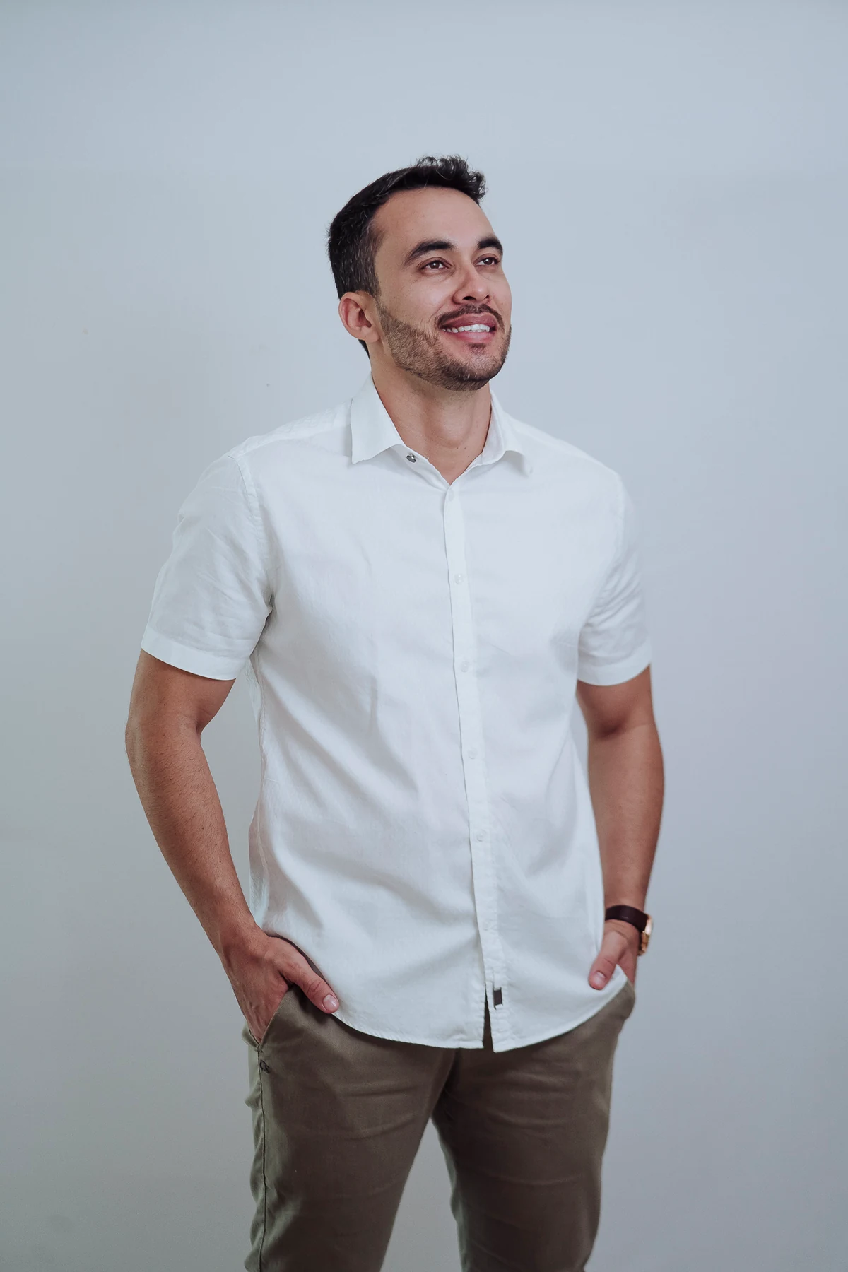 Tiago Ismar de camisa branca, sorrindo e olhando para o horizonte