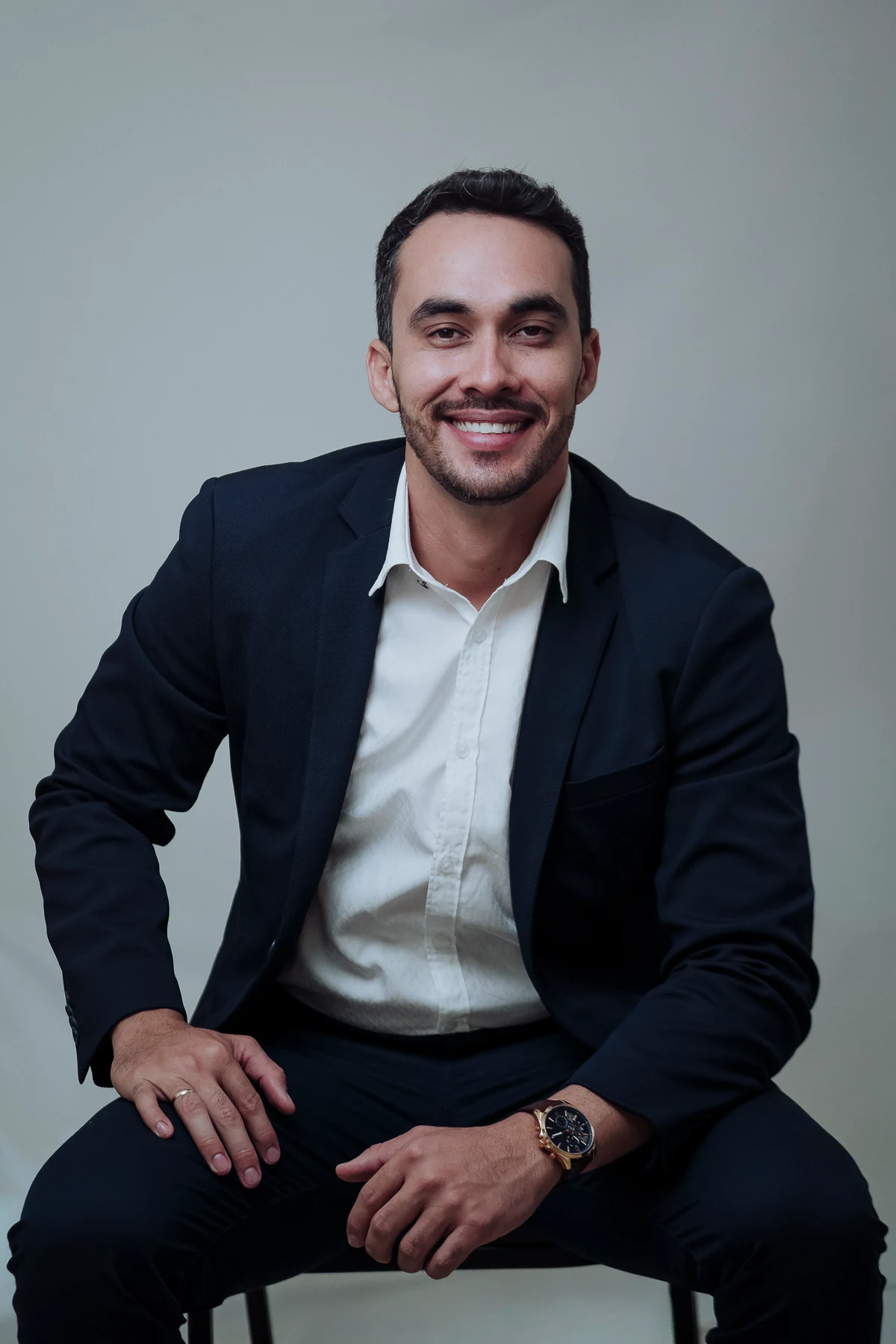 Tiago Ismar sorrindo, sentado de terno azul e camisa branca